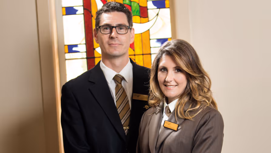 Two funeral directors in front of stained glass.