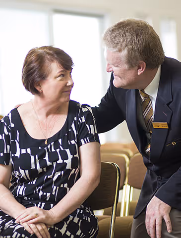 A male funeral director comforts a woman with a gentle hand on her shoulder.