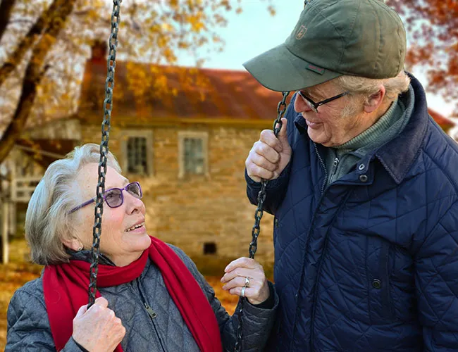 An elderly couple gazes at each other on a swing in autumn.