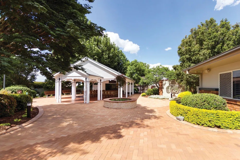 Outdoor paved area with a white gazebo and lush greenery.