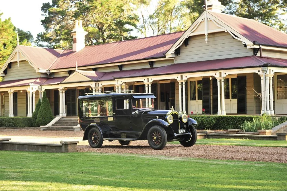 Vintage hearse parked in front of a grand house.